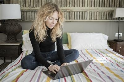 Woman using laptop computer sitting on bed at home