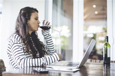 Woman using laptop while having wine at home