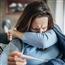 Woman coughing into her arm and holding thermometer