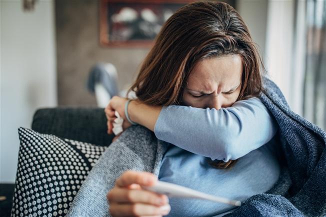 Woman coughing into her arm and holding thermometer Woman coughing into her arm and holding thermometer
