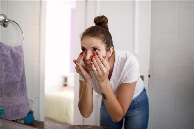 Young woman looking in bathroom mirror and touching undereye area