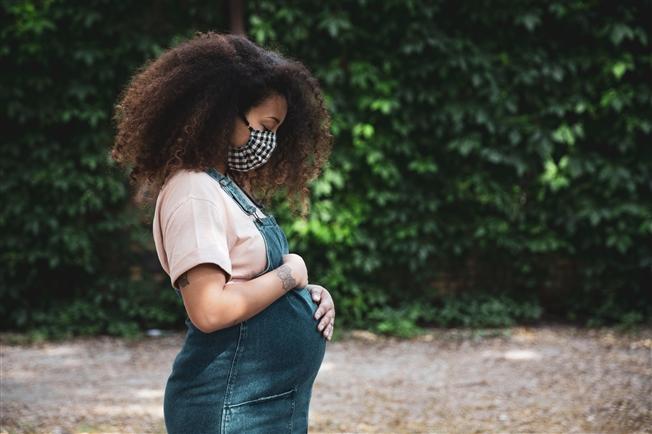 Pregnant mother COVID vaccine Young woman outdoors wearing cloth mask and cradling pregnant belly