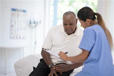 Senior Black man in doctors office reviewing medical information with health care provider