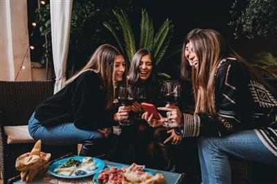 Friends drinking red wine and looking at a smartphone together Friends drinking red wine and looking at a smartphone together