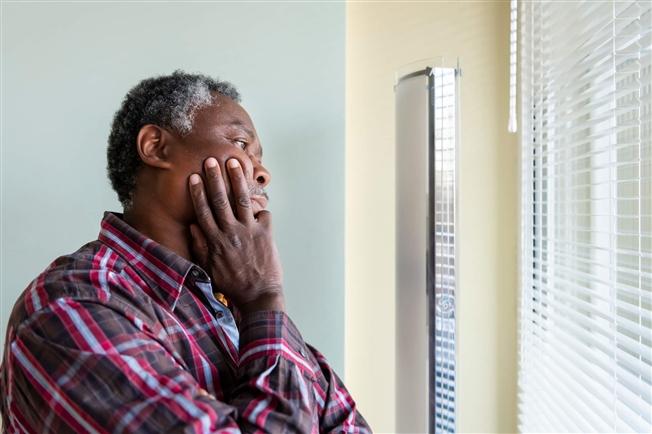 Older man in social isolation looking out window