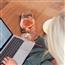 Woman drinking glass of wine while working on her computer