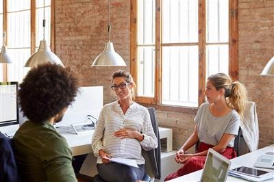 Pregnant woman talking to colleagues in office setting