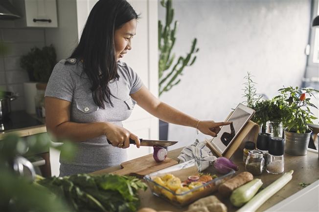 Middle aged woman cooking in kitchen reading recipe on ipad Middle aged woman cooking in kitchen reading recipe on ipad