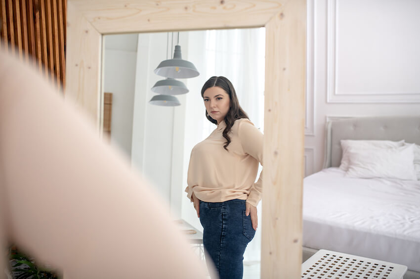 Woman observing tight-fitting clothes in mirror