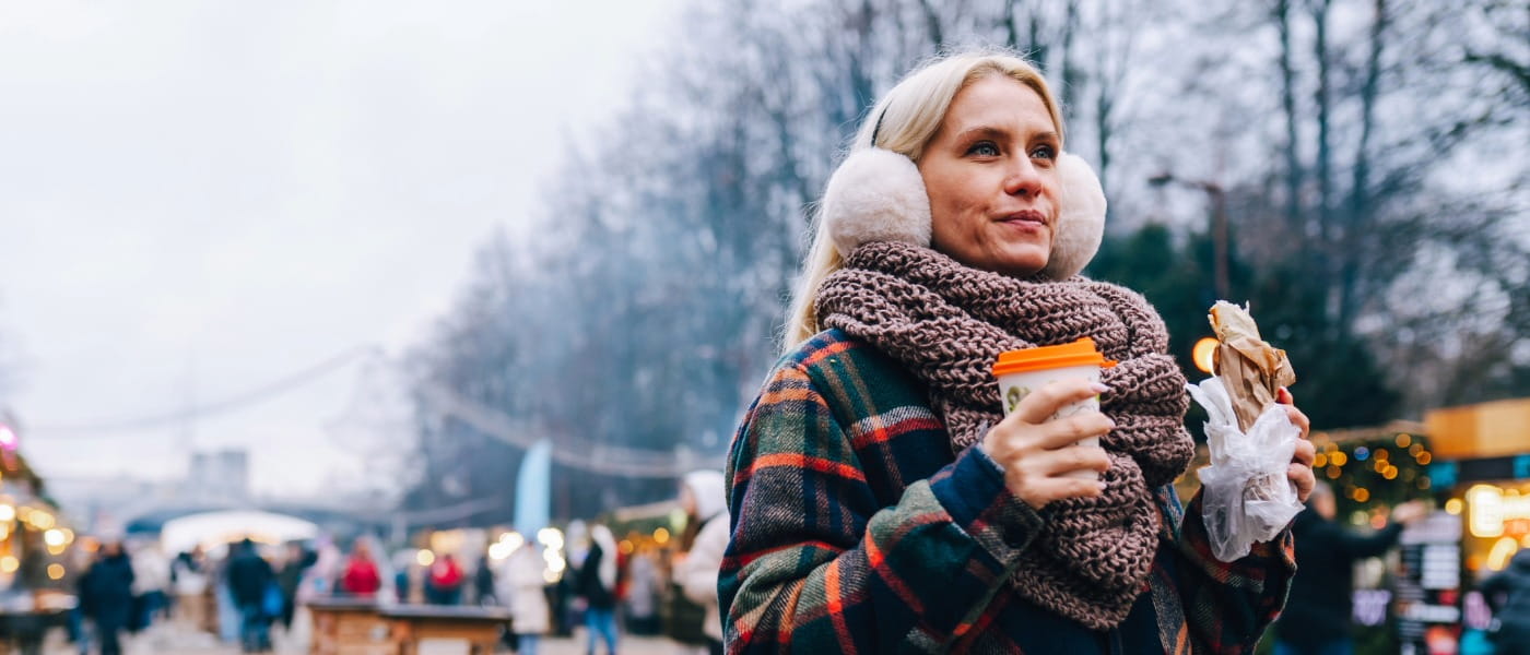 Mature woman enjoying a holiday market with hot drink and street food
