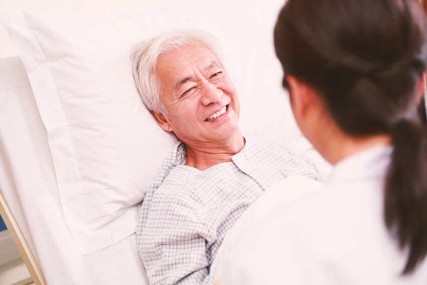 older Asian man in hospital bed being seen by doctor 