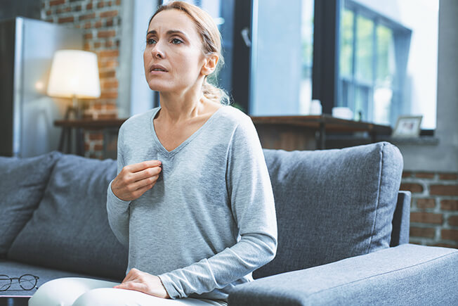 Hot flashes. Exhausted mature woman resting on sofa and having hot flash