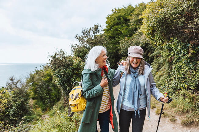 Two older women laughing together while they hike.