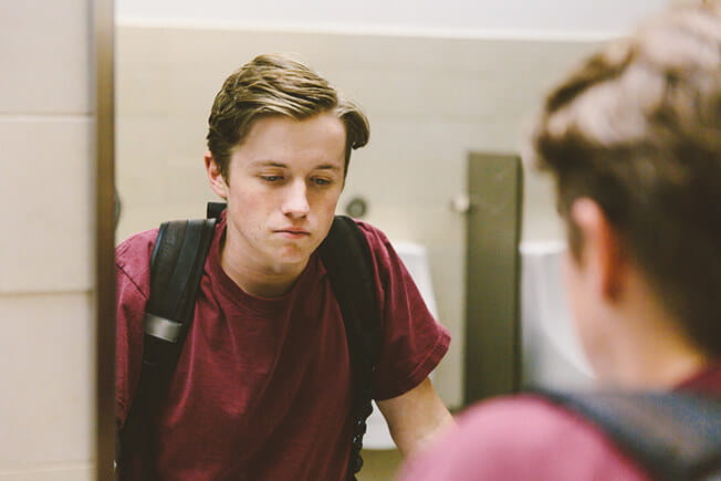 Depressed teen student looks at himself in bathroom mirror