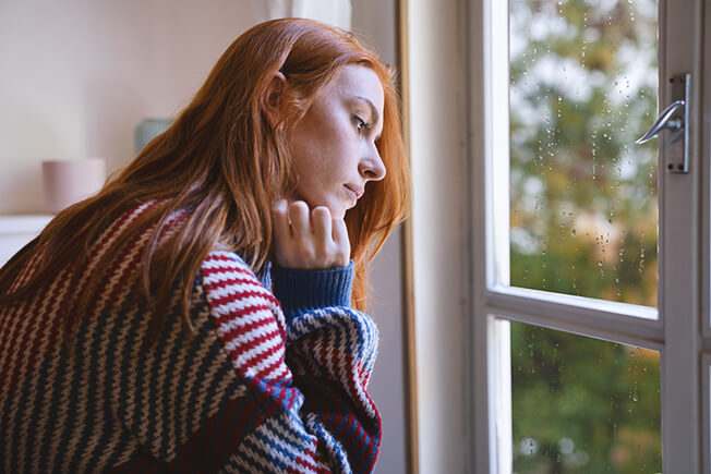 Woman with red hair looking sadly out her window.