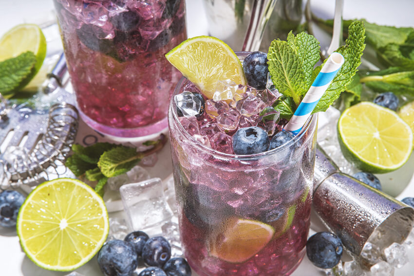 Blueberry mocktails on a table with cocktail tools and limes.