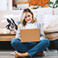 Woman sitting on the floor on her laptop with a dog on the couch behind her. 