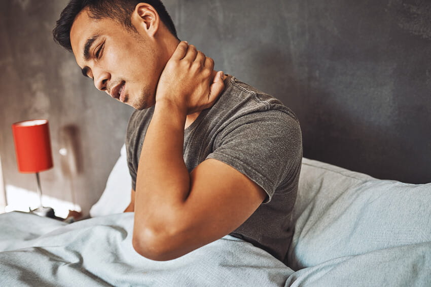 Young man in bet with his hand on his neck, looking like he's in pain. 