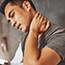 Young man in bet with his hand on his neck, looking like he's in pain. 