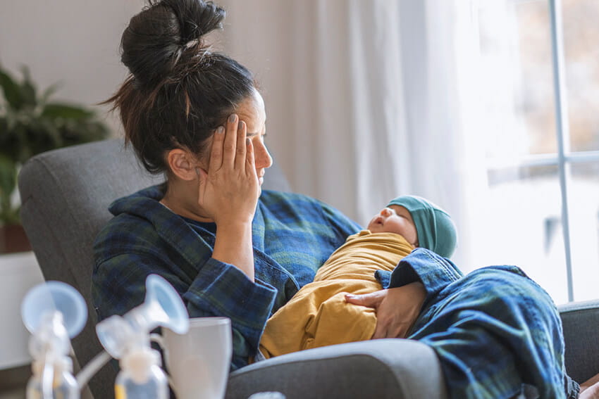 Mother with a newborn baby looking sad and stressed.