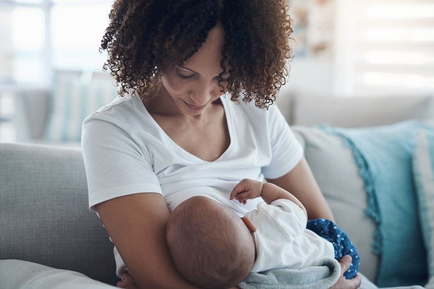 A young woman breastfeeding her baby on the sofa at home.