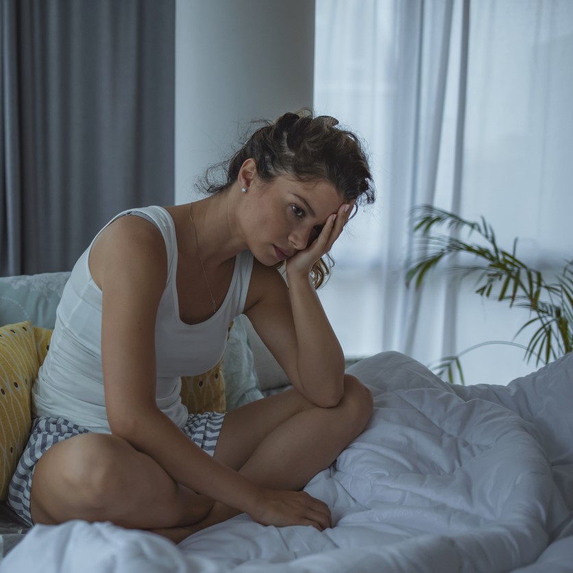 Woman sitting in bed looking unhappy.