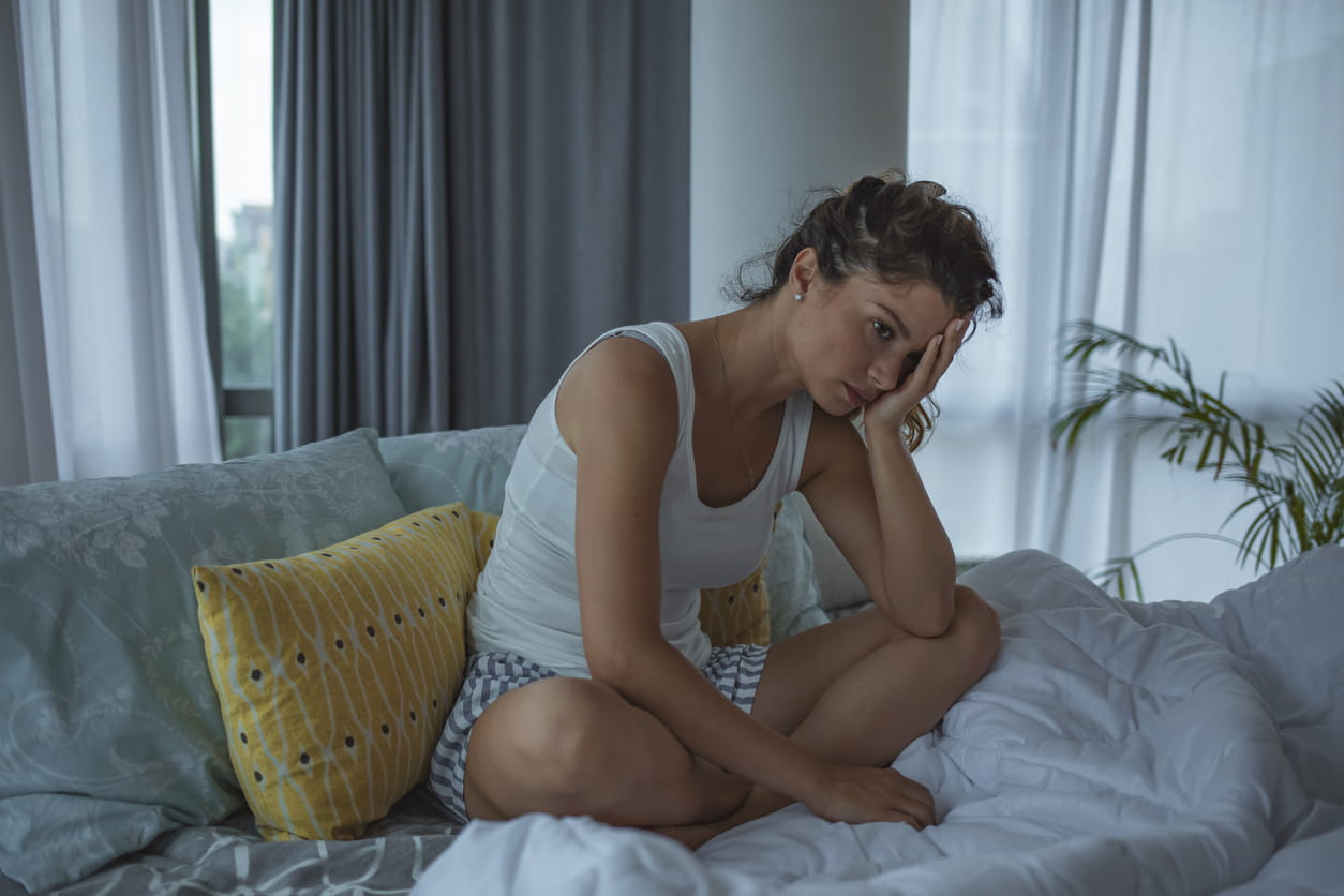 Woman sitting in bed looking unhappy.
