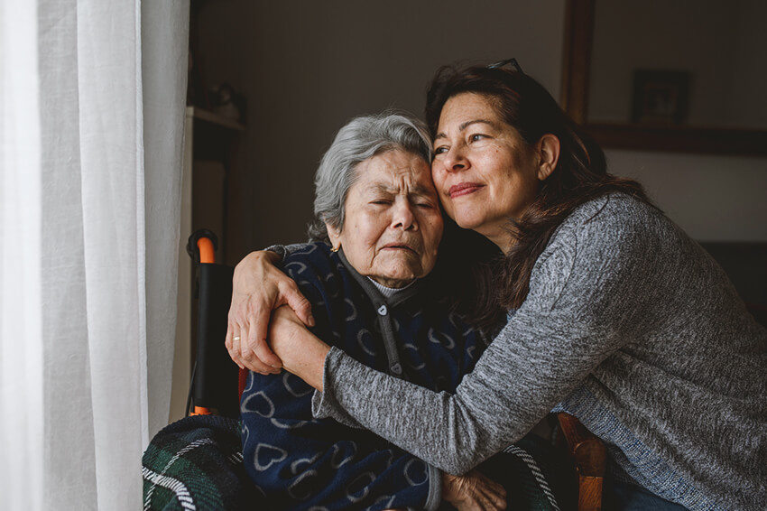 Older woman in wheelchair hugging daughter.