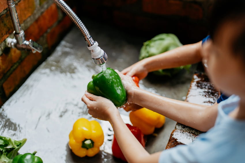 Child washing bell peppers in a sink.
