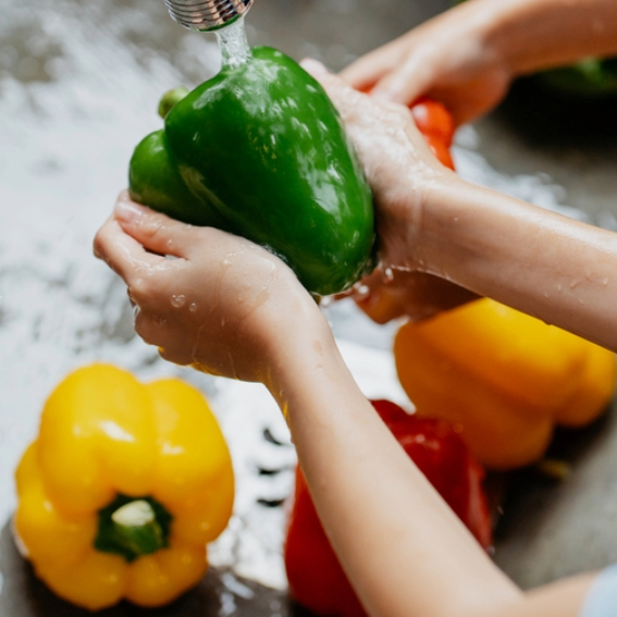 Child washing bell peppers in a sink.