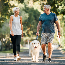 Older people walking a dog in a park.