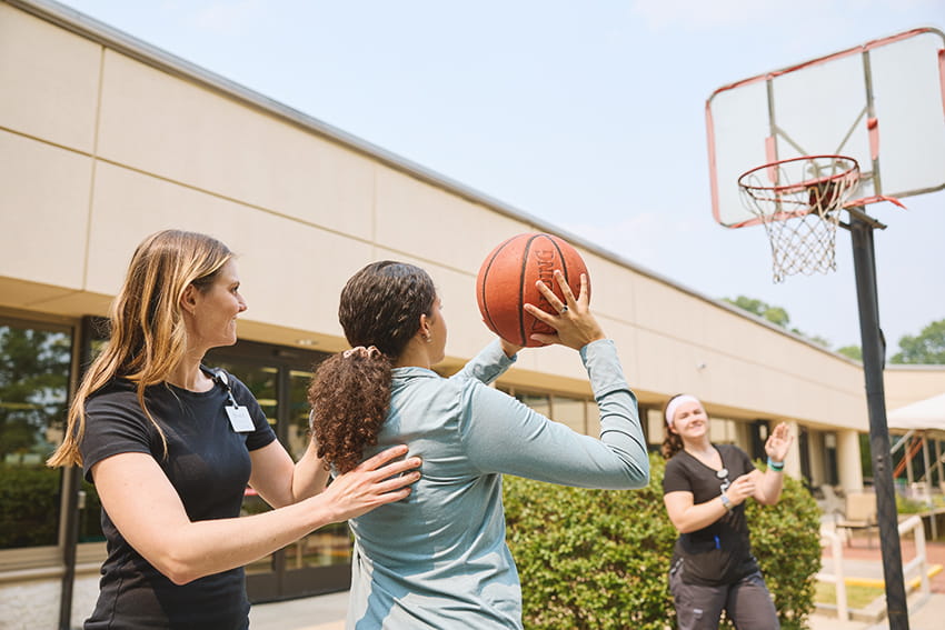 Rehab therapists assisting a patient playing basketball outside