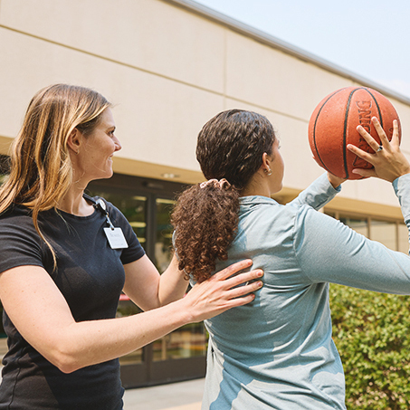 Rehab therapists assisting a patient playing basketball outside