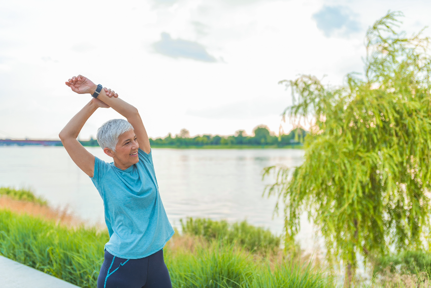 Woman smiling outside stretching hands above head.