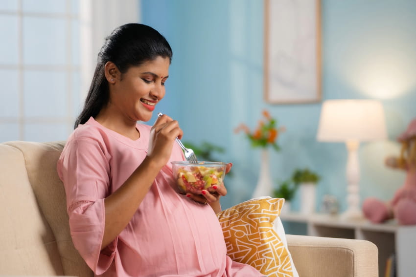 Pregnant woman eating fruit on a couch at home.