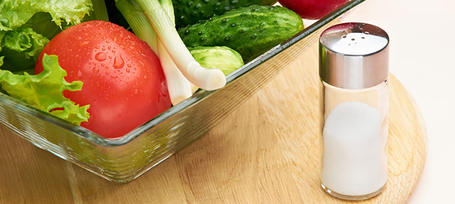 A salt shaker near a bowl of mixed vegetables.