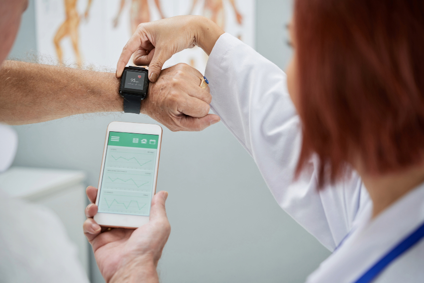 Patient with a wearable heart rate monitor and doctor helping sync it to their phone.