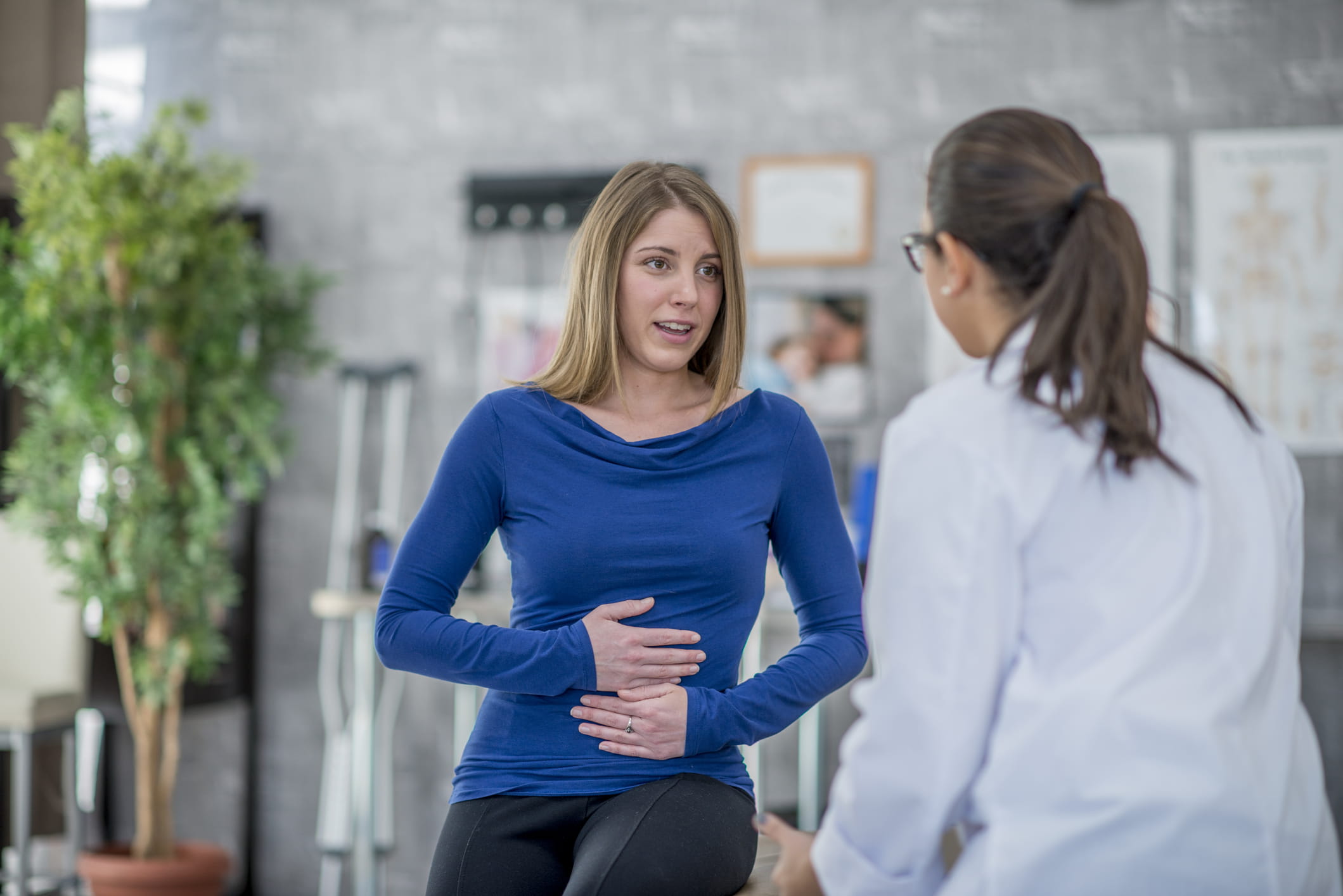 Woman holding her stomach talking to a doctor.