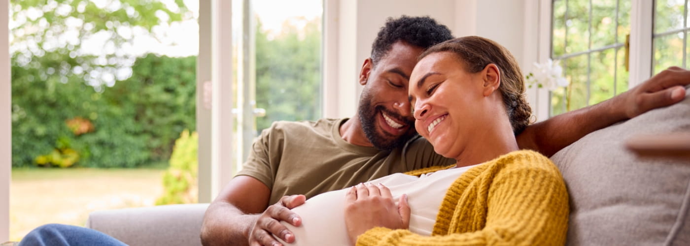 Pregnant couple sitting on the couch together at home.