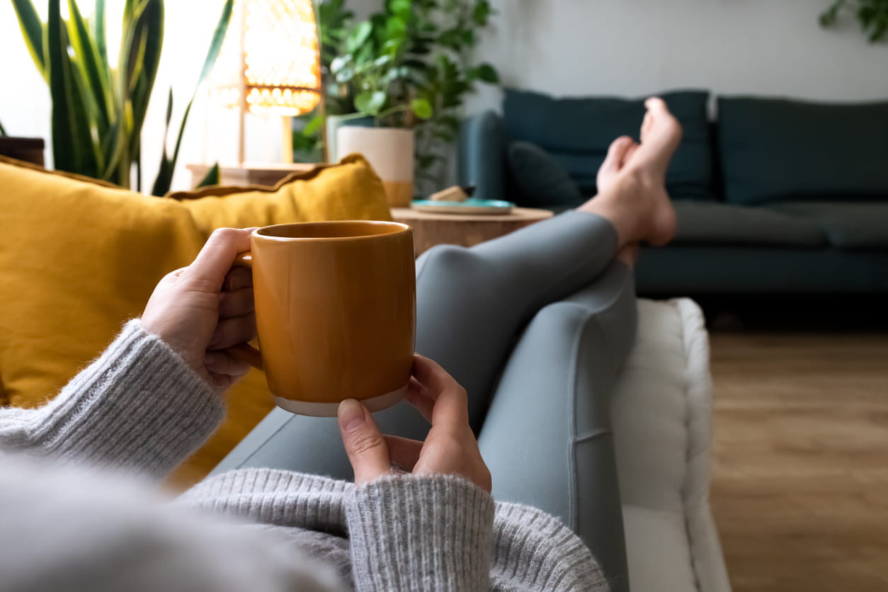 POV of young woman relaxing at home with cup of coffee lying on couch 