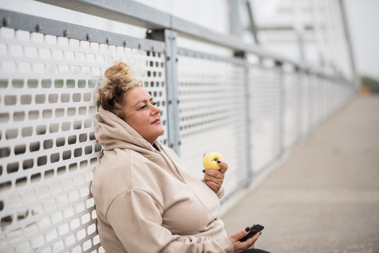 A woman sitting on a walkway eating an apple.