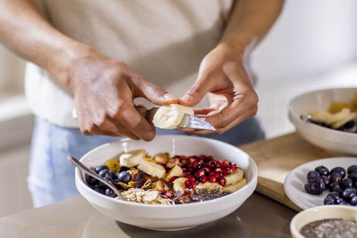 woman making healthy breakfast in kitchen with fruits and yogurt