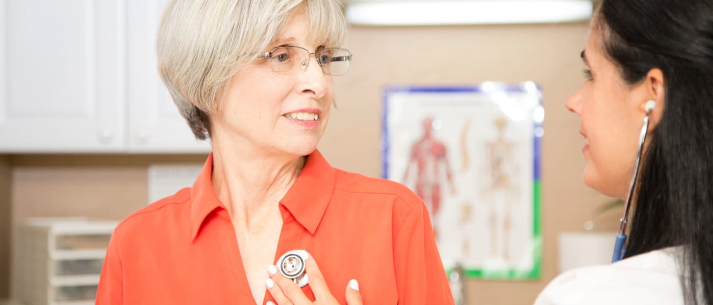 Female doctor listening to the heartbeat of a senior female patient in an exam room.