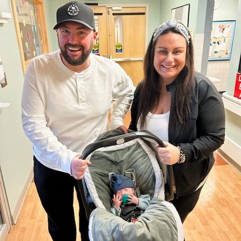 Gabrielle and her partner holding Luca in his baby carrier