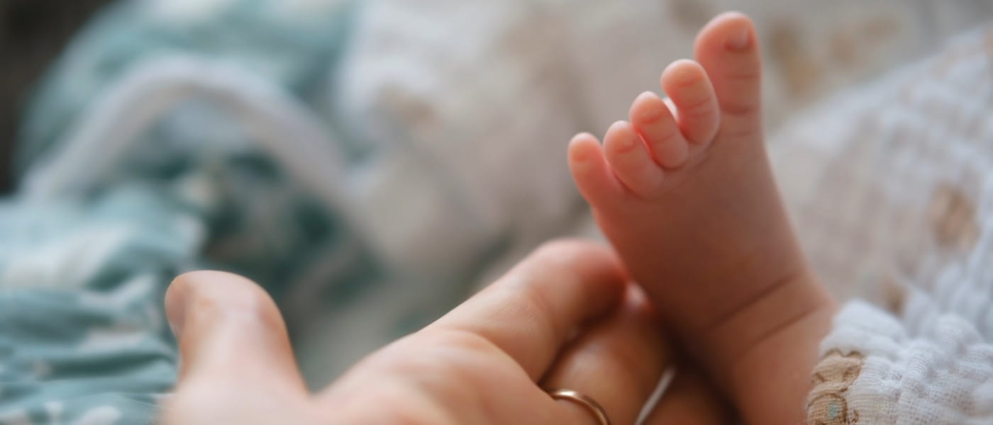 A mother gently holds the tiny foot of her newborn baby