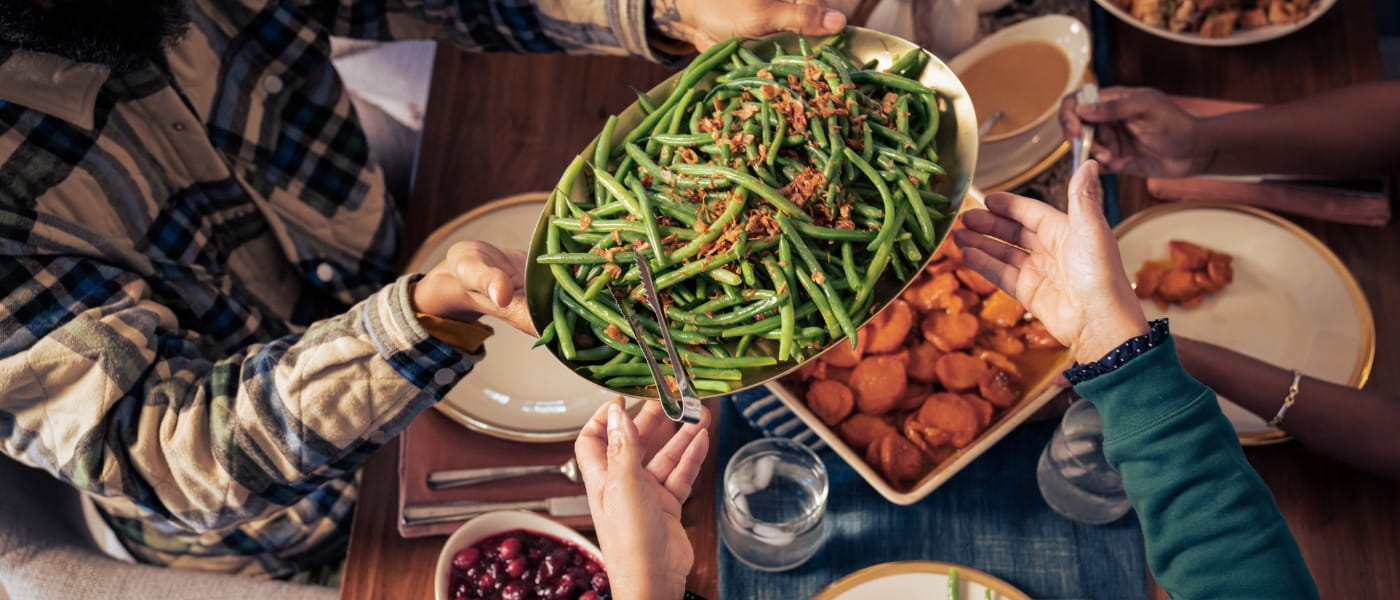 two adults' hands passing a platter of green beans over a table set for Thanksgiving