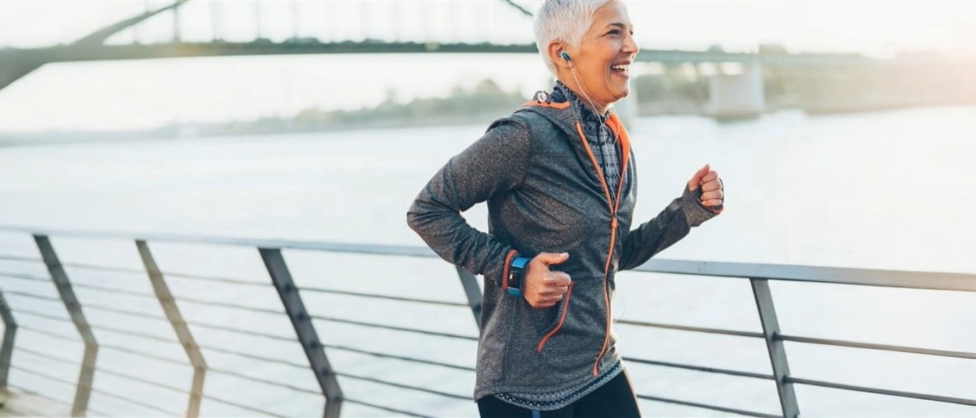 Athletic senior woman running along a river and bridge while wearing a smartwatch