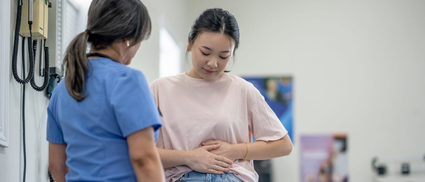 A young woman sits up on an exam table as she talks with her female doctor about her lower abdominal pain.