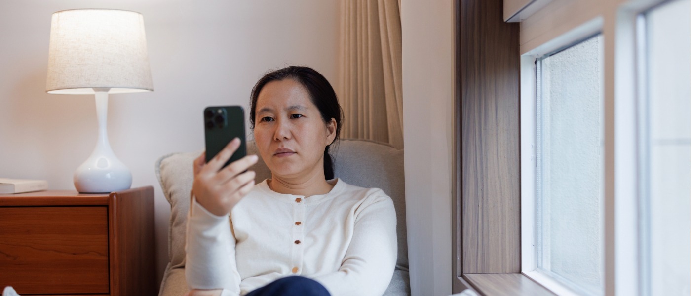 A middle-aged woman looking at her mobile phone with a look of concern on her face.