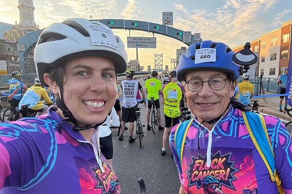 Emily Levy, MD, and her father in their racing gear under an arch on the Ben Franklin Bridge in Philadelphia, PA before the start of the American Cancer Society Bike-A-Thon.